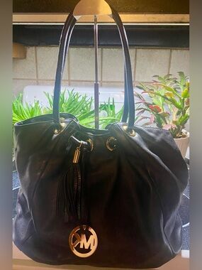 Michael Kors black leather handbag features a prominent gold circular logo charm